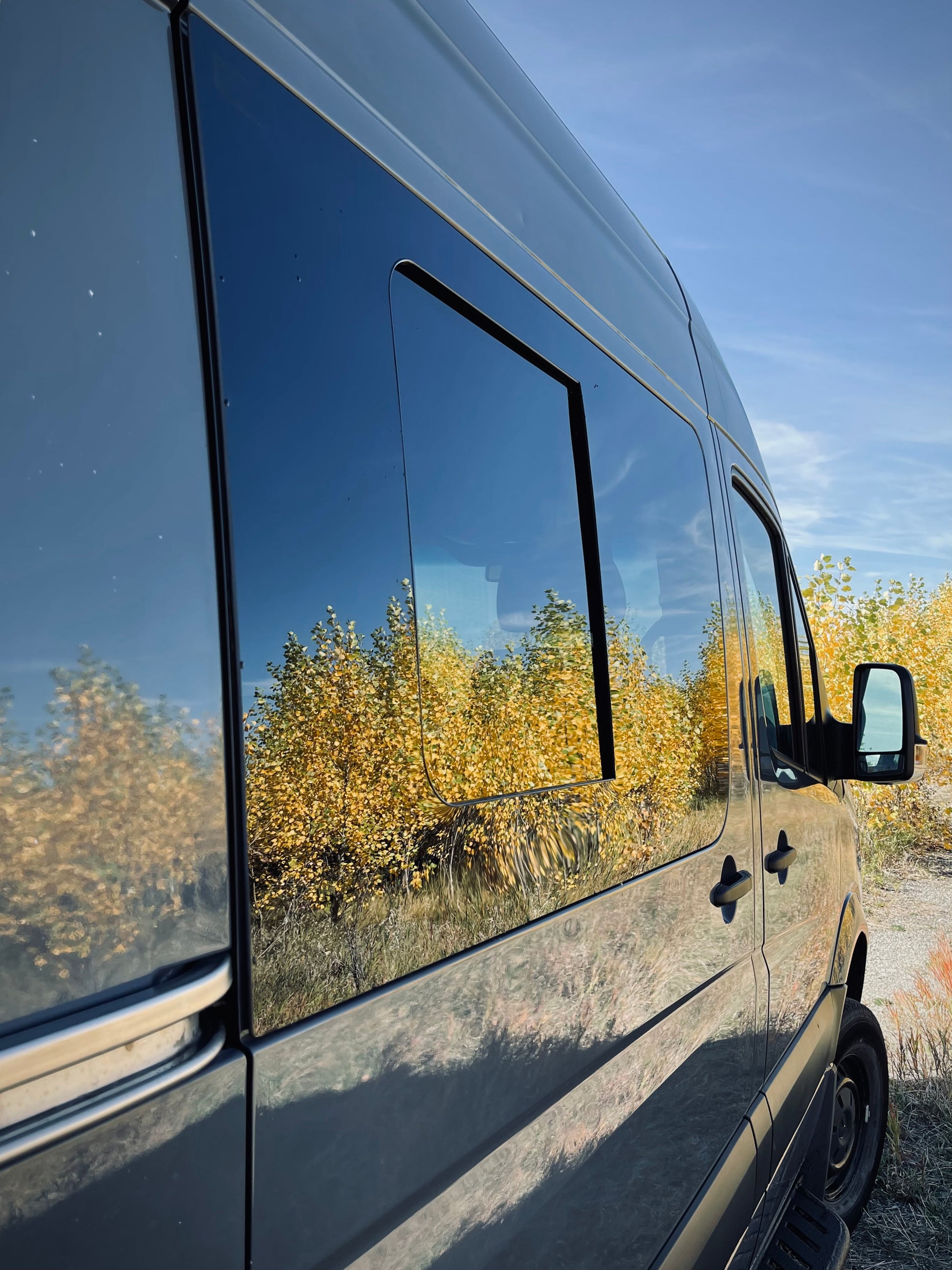 Exterior side view of custom van windows showing the reflection of trees.