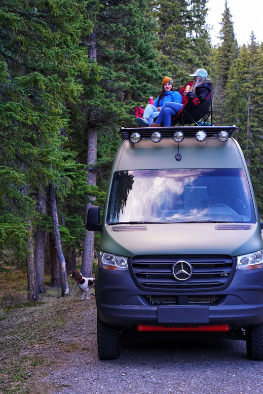 Two people sitting in a camping chair on top of their Sprinter roof rack.